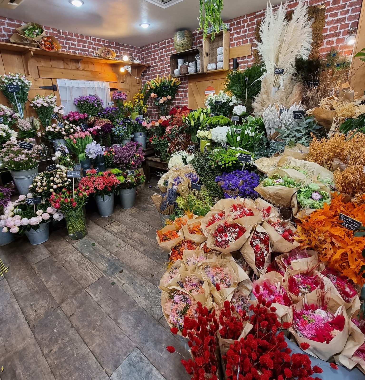 L’intérieur : seaux de fleurs fraîches, bouquets de fleurs séchées et mur de briques